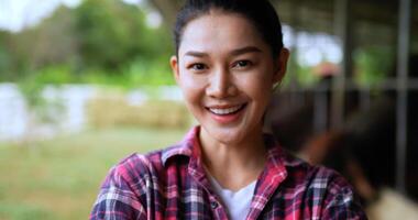 Attractive portrait headshot of farmer young woman plaid shirt and jeans standing crossed her arms, smile and looking to camera in cattle farm video