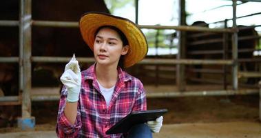 asiatische attraktive landwirtschaftliche Viehzüchterin verwendet digitalen Stift, um auf dem Tablet zu schreiben, während sie Tiere auf dem Bauernhof überprüft