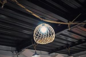 Bottom view of yellow bulb with rattan woven ornament that hanging in the rope. Inspiration for modern lighting and home decoration. Rattan chandelier for vintage and abstract background. Wicker Lamp. photo