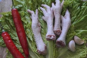 Raw chicken feets on a chopping Board with lettuce, red chilies, and garlics. Fresh and organic chicken feets. Top view photo