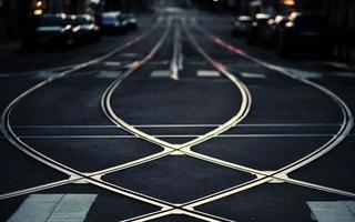 Photo of crossed white steel railroad tracks on the road paved with black asphalt with black background and has a car in the background