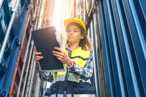 Women Engineer wears PPE checking container storage with cargo container background at sunset. Logistics global import or export shipping industrial concept. photo