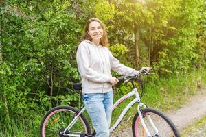 mujer joven montando en bicicleta en el parque de la ciudad de verano al aire libre. gente activa chica hipster relajarse y andar en bicicleta foto