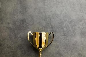 Simply flat lay design winner or champion gold trophy cup on concrete stone grey background. Victory first place of competition. Winning or success concept. Top view copy space. photo