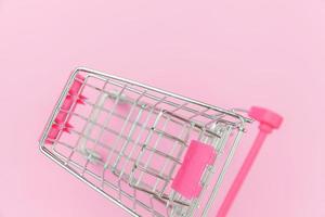 Small supermarket grocery push cart for shopping toy with wheels isolated on pink pastel colorful trendy background. Sale buy mall market shop consumer concept. Copy space. photo