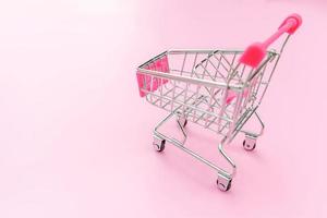 Small supermarket grocery push cart for shopping toy with wheels isolated on pink pastel colorful trendy background. Sale buy mall market shop consumer concept. Copy space. photo