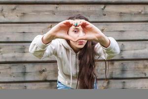 Love, heart shape, peace. Beauty portrait young happy positive woman showing heart sign with hands on wooden wall background photo