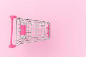 Small supermarket grocery push cart for shopping toy with wheels isolated on pink pastel colorful trendy background. Sale buy mall market shop consumer concept. Copy space.