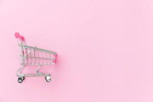 Small supermarket grocery push cart for shopping toy with wheels isolated on pink pastel colorful trendy background. Sale buy mall market shop consumer concept. Copy space. photo