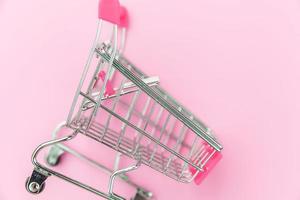 Small supermarket grocery push cart for shopping toy with wheels isolated on pink pastel colorful trendy background. Sale buy mall market shop consumer concept. Copy space.