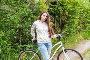 mujer joven montando en bicicleta en el parque de la ciudad de verano al aire libre. gente activa chica hipster relajarse y andar en bicicleta foto