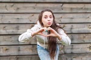 Love, heart shape, peace. Beauty portrait young happy positive woman showing heart sign with hands on wooden wall background photo