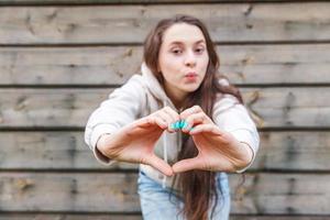 Love, heart shape, peace. Beauty portrait young happy positive woman showing heart sign with hands on wooden wall background photo
