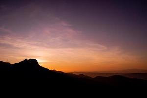 romántica puesta de sol púrpura y naranja sobre las altas montañas tatra con densa niebla y largos rayos de sol. amanecer vibrante y colorido desde el pico. trekking durante la hora dorada en el bosque. foto