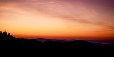romántica puesta de sol púrpura y naranja sobre las altas montañas tatra con densa niebla y largos rayos de sol. amanecer vibrante y colorido desde el pico. trekking durante la hora dorada en el bosque. foto