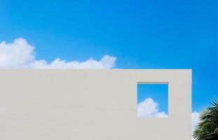 Exterior Wall concrete texture with open window and coconut palm leaf against blue sky and clouds, White paint cement building, Modern architecture with square frame in Spring or Summer sky photo