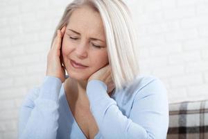 Woman suffering from stress or a headache grimacing in pain as she holds the back of her neck with her other hand to her temple, with copyspace. Concept photo with indicating location of pain.