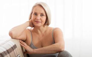 Active beautiful middle-aged woman smiling friendly and looking in camera in living room. Woman's face close up. Realistic images without retouching with their own imperfections. Selective focus. photo