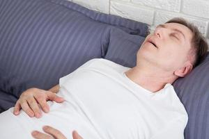 Man snoring because of sleep apnea lying in the bed photo