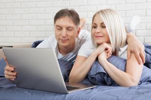 Smiling attractive couple lying on bed using laptop communicating online at home, happy man and woman typing on computer, enjoying internet shopping or chatting in social networks in bedroom. photo