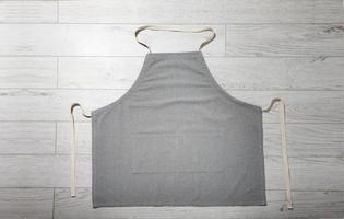 Gray apron for kitchen top view on white wooden background. photo