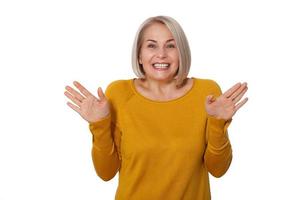 Middle aged blonde emotionally posing in a studio. Happy woman in yellow bright sweater on white background photo