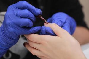 Master in protective gloves during a manicure at beauty salon. Master manicurist varnishes the marsala gel on the nails of a female client. The concept of beauty and health. photo
