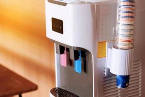 Detail of the two plastic taps for hot and cold water, colour coded, on a electric purified water dispenser. Modern water cooler with paper cups in office. Healthcare concept. Business concept photo
