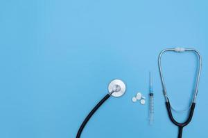 estetoscopio, pastillas blancas y jeringa sobre fondo azul. medicamentos concepto de atención médica. copie el espacio foto