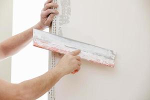 constructor en máscara protectora usando una paleta para agregar yeso. enlucido de pared con espátula, imagen de primer plano. fijación de la superficie de la pared y preparación para pintar. trabajos de construcción durante la cuarentena foto