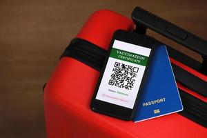 New normal concept. Close up view of a smartphone with an immune digital health passport, a red suitcase, and passport. Traveling by plane during a pandemic. Protection from disease photo