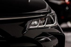 headlight of modern prestigious black car close up. Close up photo of modern car, detail of headlight. Headlight car Projector LED of a modern luxury technology and auto detail