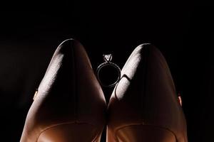 Golden ring with diamond between pair of bride shoes on dark background. selective focus photo