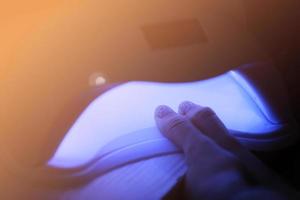 Closeup view of female hands with gel polish manicure. Woman puts hand into led uv lamp for curing top cover of nailpolish. UV lamp, LED Nail photo