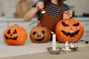 niña enciende una vela para halloween. niña en traje de bruja con calabaza tallada con una cara hecha por un niño. familia feliz preparándose para halloween. enfoque selectivo foto