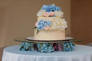 white wedding cake with blue hydrangeas and pink roses flowers on the table. Stylish flowers wedding day. photo