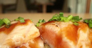 Cebollino verde picado encima de rollos de sushi de salmón en un restaurante de sushi - macro video