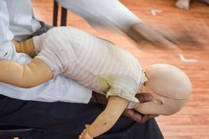 hombre realizando RCP en un maniquí de muñeca de entrenamiento para bebés con compresión con una mano. formación en primeros auxilios - reanimación cardiopulmonar. curso de primeros auxilios en maniquí de cpr, concepto de capacitación en primeros auxilios de cpr foto