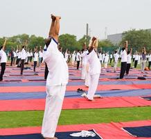 New Delhi, India, June 21 2022 - Group Yoga exercise session for people at Yamuna Sports Complex in Delhi on International Yoga Day, Big group of adults attending yoga class in cricket stadium photo