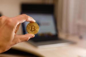 moneda de oro bitcoin en la mano del hombre en el fondo de la computadora portátil en una mesa blanca foto