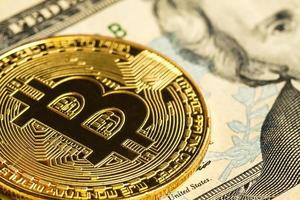 bitcoin de oro sobre un fondo blanco junto a nosotros papel moneda con un valor nominal de dólares foto