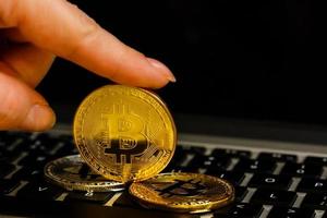 Golden bitcoin in fingers with the laptop keyboard background crypto currency concept photo
