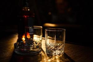 Glasses of whiskey with smoking cigar and ice cubes on wooden table photo