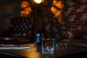 Glasses of whiskey with smoking cigar and ice cubes on wooden table photo