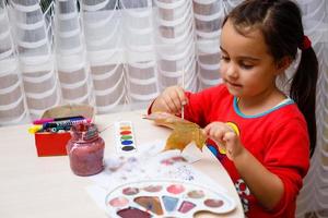 niña pintando sobre hojas amarillas de otoño con gouache artes infantiles creatividad infantil arte otoñal foto