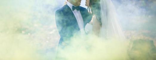 Wedding couple posing near rocks with colored smoke behind them photo