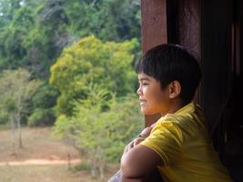 boy looking out window looking at the green forest photo