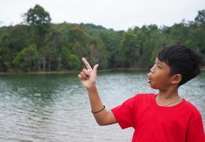 The boy smiled and pointed his hand to his side. On the background is a reservoir. photo