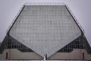 Hugging wedding couple stands hidden under the veil before glass house photo