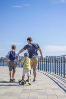 Children and a man walk across the bridge and look at the river. Various interesting things are attached to the railing. A hot summer day photo